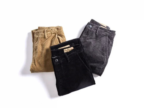 Three pairs of folded corduroy pants in tan, black, and charcoal gray, arranged on a clean white background.