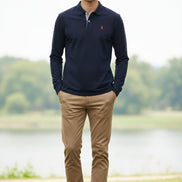 Navy long-sleeve polo shirt with a small red logo on a rack with other colored shirts.