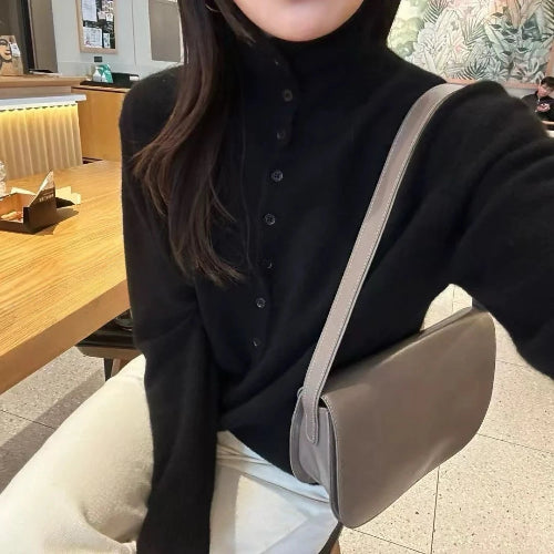 Person wearing a black shirt with a beige crossbody bag in an indoor setting