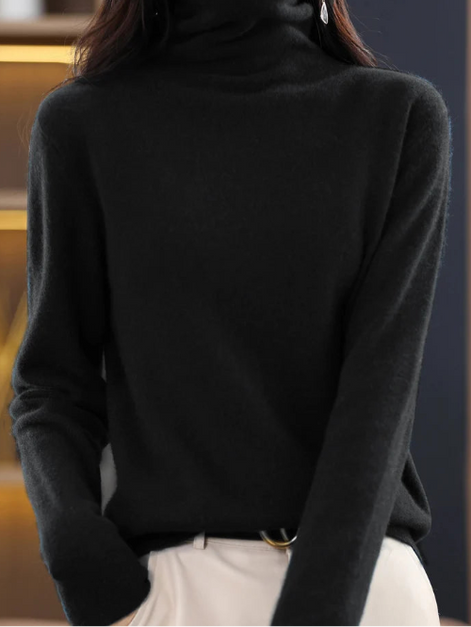 A woman wearing a black long-sleeve turtleneck sweater, paired with off-white pants, shown from the neck down in a close-up shot.