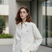 Person wearing a white shirt with a blue heart emblem on a plain background