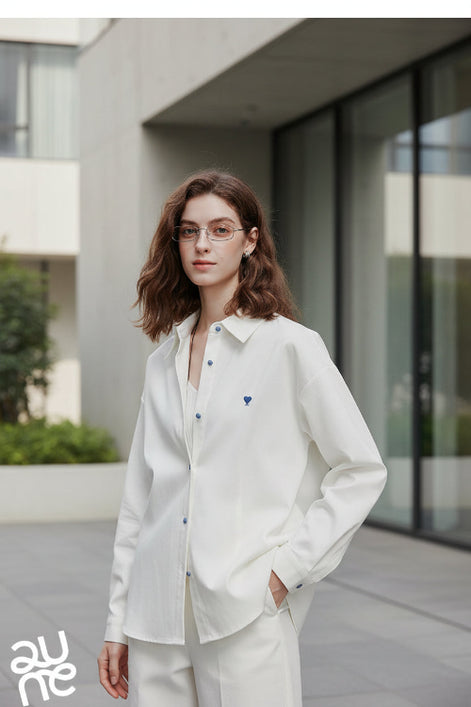 Person wearing a white shirt with a blue heart emblem on a plain background