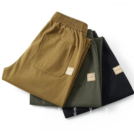 Folded khaki, army green, and black pants showing elastic waistbands, back patch pockets, and small sewn-on labels.