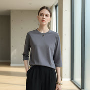 Person wearing a gray sweater and black pants, holding a white handbag indoors.