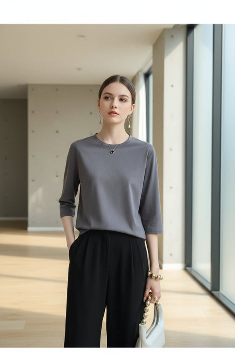 Person wearing a gray sweater and black pants, holding a white handbag indoors.