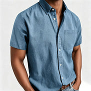A man wearing a short-sleeve button-down shirt in a dusty blue chambray fabric, paired with brown leather belt and light 