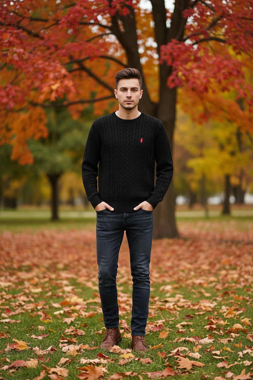 Black cable knit sweater with a red logo on a hanger against a wooden background