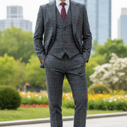 Man wearing a gray checkered suit with a red patterned tie in front of a blurred cityscape.