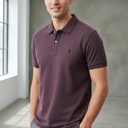 Purple polo shirt with a brand logo held by a hand, with other shirts in the background.
