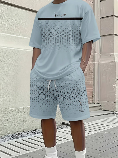 A man wearing a light blue matching t-shirt and shorts set with a geometric pattern, standing outdoors against a beige brick wall.