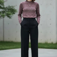 A woman wearing a marled knit mock-neck sweater in a dusty rose and burgundy tone, paired with a black skirt, standing in front of a softly lit window.