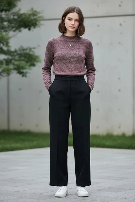 A woman wearing a marled knit mock-neck sweater in a dusty rose and burgundy tone, paired with a black skirt, standing in front of a softly lit window.