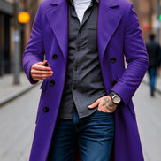 A man wearing a vibrant purple double-breasted overcoat over a dark gray button-up shirt, white t-shirt, and blue jeans, standing on a city street.