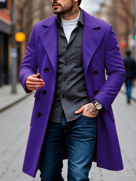 A man wearing a vibrant purple double-breasted overcoat over a dark gray button-up shirt, white t-shirt, and blue jeans, standing on a city street.