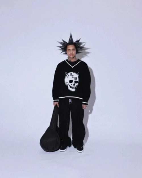 Front view of a model wearing black wide-leg jeans with a black skull-design top, holding a black guitar case against a pale background.