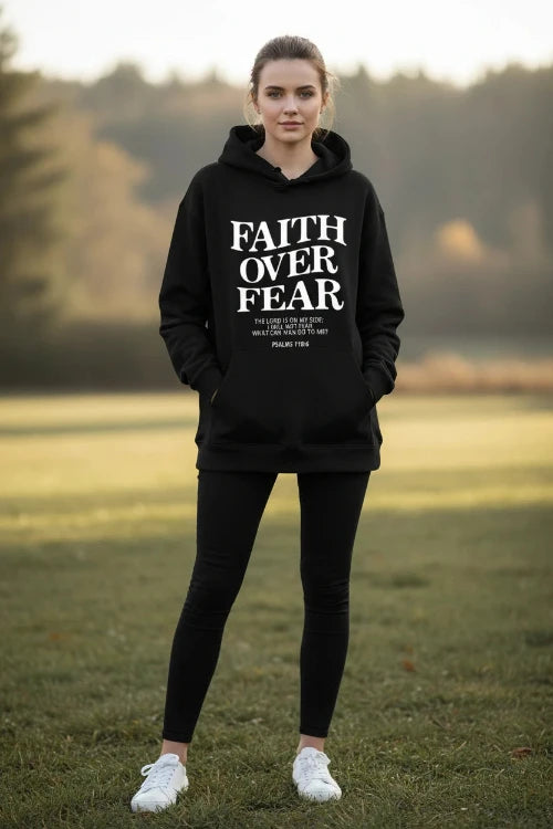 Black hoodie with 'Faith Over Fear' text on a wooden surface with shoes and headphones.