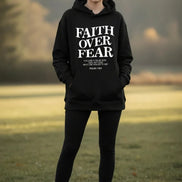 Black hoodie with 'Faith Over Fear' text on a wooden surface with shoes and headphones.