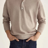 Man wearing a beige long-sleeve polo shirt and dark jeans on a plain background