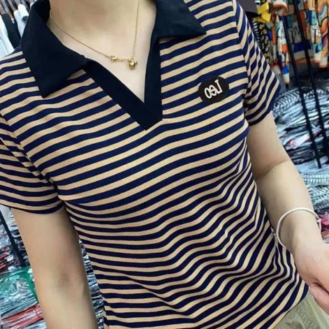 A close-up of a person wearing a short-sleeve polo shirt with navy blue and beige horizontal stripes, featuring a solid navy collar and a small white embroidered logo on the chest.