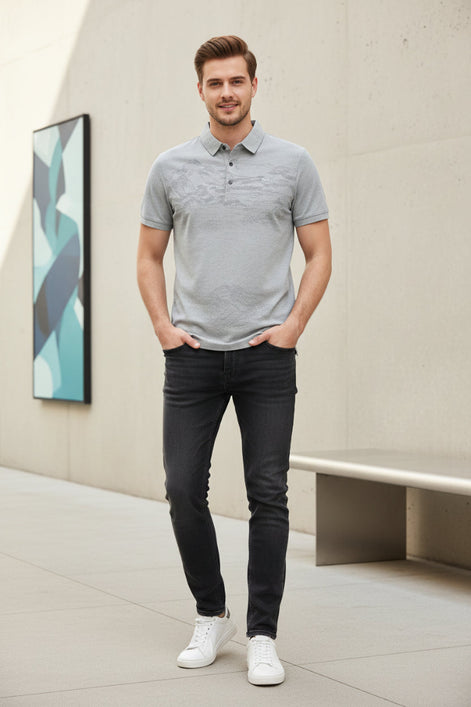 A light gray short-sleeve polo shirt with a subtle landscape print on the front and a small chest logo, shown on a black hanger with a hand holding the sleeve to demonstrate fabric texture.
