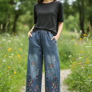 Person wearing blue denim pants with floral embroidery in a room setting.
