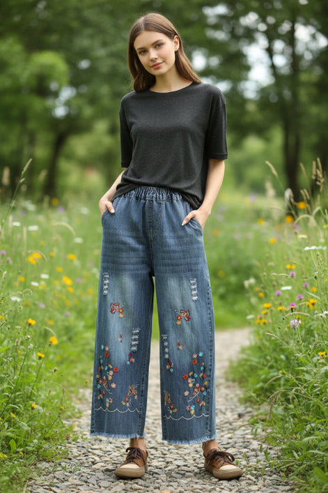 Person wearing blue denim pants with floral embroidery in a room setting.
