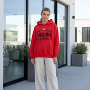A bright red pullover hoodie laid flat on a dark textured surface, featuring a black 'family CHRISTMAS 2026'