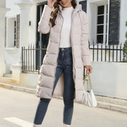 Woman wearing a long puffer coat, white top, blue jeans, and white boots in an urban setting.
