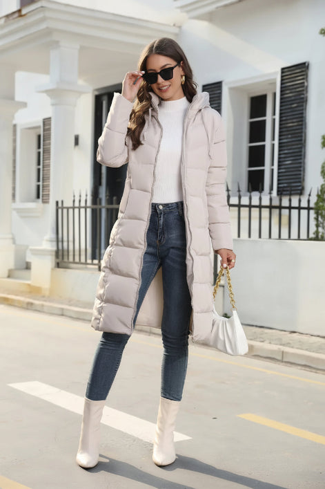 Woman wearing a long puffer coat, white top, blue jeans, and white boots in an urban setting.