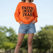Orange sweatshirt with 'Faith Over Fear' text on a wooden background