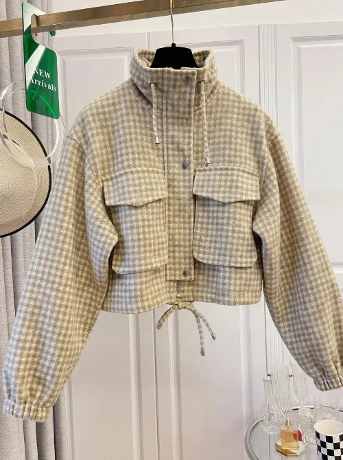 Beige and cream checked utility jacket on a hanger, showing a raised drawcord collar, chest flap pockets, front snap buttons, elasticated cuffs and a tied drawcord hem