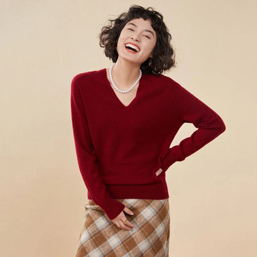 Woman wearing a red sweater and plaid skirt against a beige background