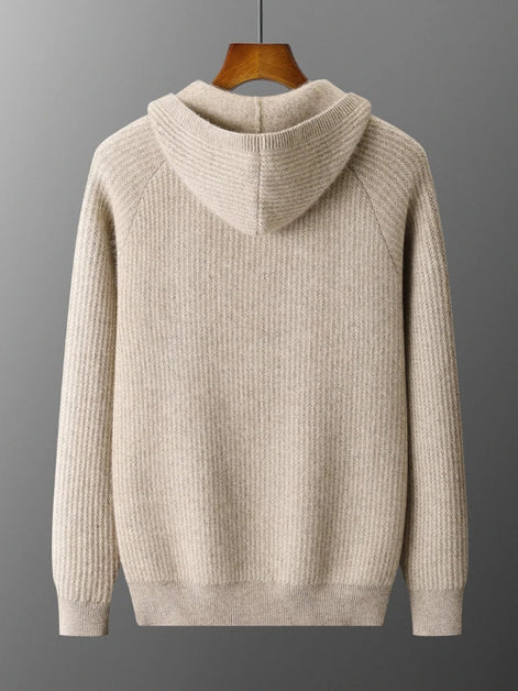 A light beige ribbed knit hooded sweater hanging on a wooden hanger against a dark gray gradient background.