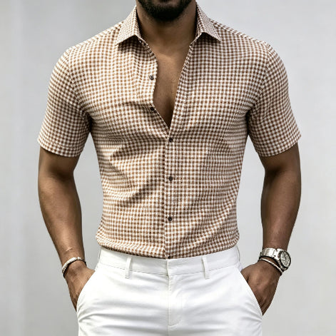 A man wearing a brown and beige gingham short-sleeve button-up shirt tucked into white trousers, 