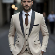 Man wearing a beige suit with black lapels and a brown tie against a blurred background