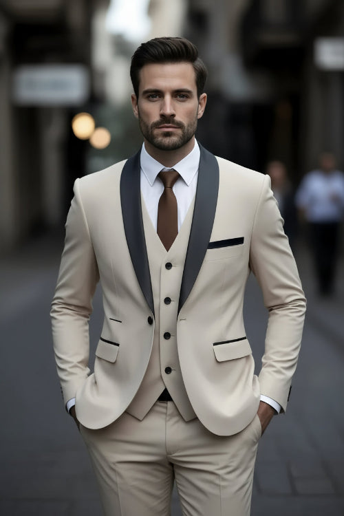 Man wearing a beige suit with black lapels and a brown tie against a blurred background