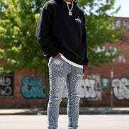 Distressed blue jeans worn with white sneakers on a light gray background