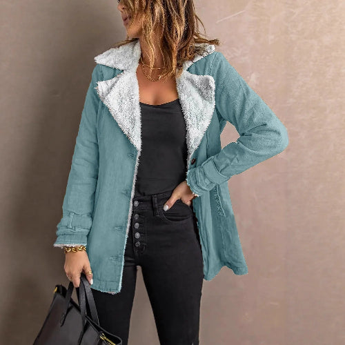 Woman wearing a light blue jacket with white fleece-look lining, wide lapels and buckled cuffs over a black top and jeans