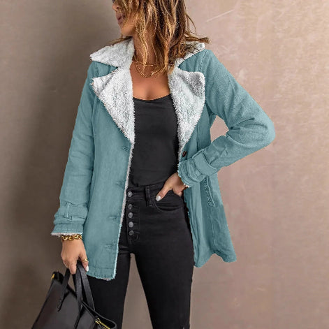 Woman wearing a light blue jacket with white fleece-look lining, wide lapels and buckled cuffs over a black top and jeans