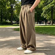 Brown herringbone wide-leg pants worn by a man standing in a park