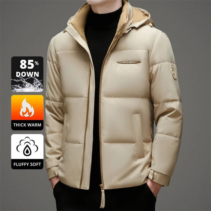 A man wearing a beige hooded puffer jacket over a black turtleneck, shown from the neck down against a gray studio background. Three feature callout graphics appear on the left side, highlighting down insulation, thick warmth, and fluffy soft texture.