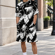 A person wearing a matching black and white abstract print t-shirt and shorts set with a musical note pattern, standing outdoors against a light-colored stone wall.