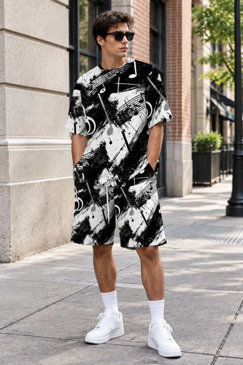 A person wearing a matching black and white abstract print t-shirt and shorts set with a musical note pattern, standing outdoors against a light-colored stone wall.