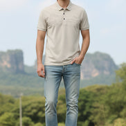 A men's short-sleeve polo shirt in a light beige or cream color, featuring a subtle, tonal landscape graphic across the chest. The shirt is displayed on a black hanger against a solid white background.