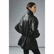 Rear three-quarter view of a woman wearing a black faux leather jacket with a raised collar and gathered waist
