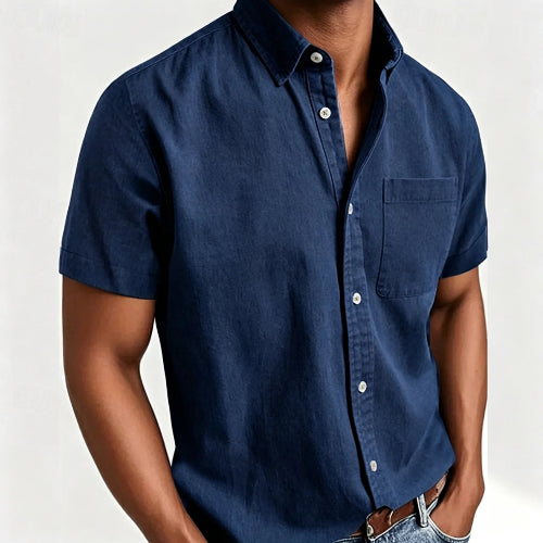A man wearing a dark navy blue short-sleeve button-down shirt with a chest pocket, paired with blue jeans and a brown leather belt,