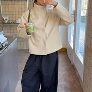 Woman wearing a cream double-breasted short coat with black trousers in a café