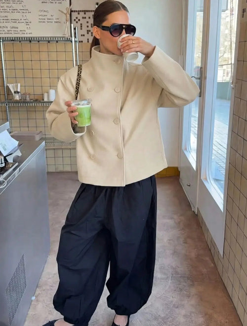 Woman wearing a cream double-breasted short coat with black trousers in a café
