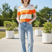 A woman wearing a short-sleeve knit polo shirt with bold horizontal orange and off-white stripes, seated on a dark brown leather chair.