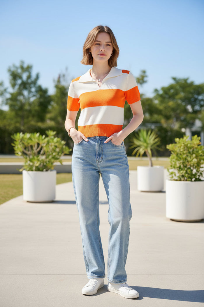 A woman wearing a short-sleeve knit polo shirt with bold horizontal orange and off-white stripes, seated on a dark brown leather chair.